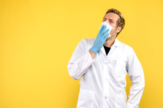 面具正面图黄色背景上戴着口罩打呵欠的男医生-医疗卫生大流行医疗专业实验室