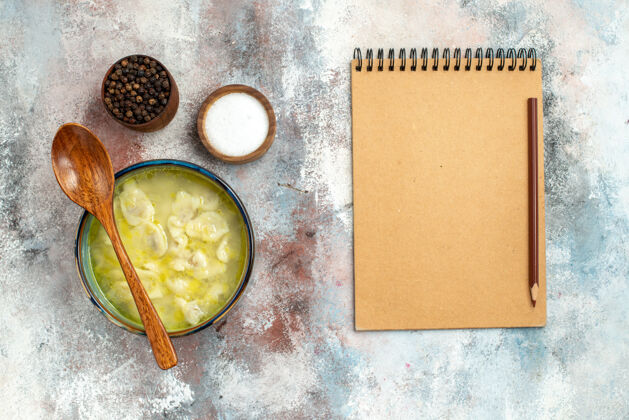 观点俯瞰杜什巴拉饺子汤碗 汤碗上放着盐胡椒木勺 笔记本和铅笔放在裸体表面笔记本铅笔年龄