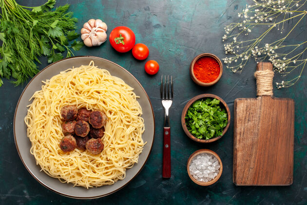 烹饪在深蓝色的桌子上俯瞰煮熟的意大利面食和肉丸调味料以及绿色蔬菜肉丸面团晚餐