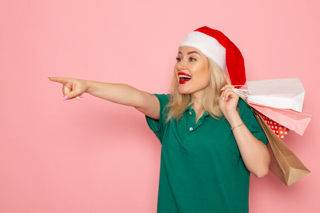 风景正面图：年轻女性手持圣诞礼物 包装在粉色墙壁上 节日模型 圣诞节 新年颜色色彩微笑肖像