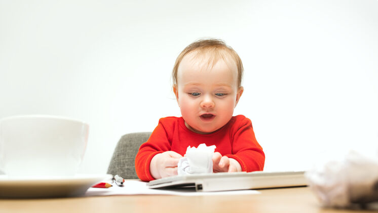 童年快乐的小女婴坐在一个白色的工作室里 用现代电脑或笔记本电脑的键盘科技年轻房子