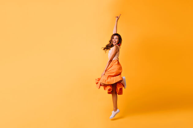 卷发一个穿着橘色裙子和白色鞋子的漂亮女孩的摄影棚镜头兴奋的红发女士跳上黄色的裙子狂喜有趣裙子