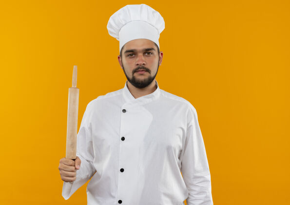 复制身着厨师制服的年轻男厨师手拿擀面杖 看上去孤立在橙色的空间里年轻寻找别针