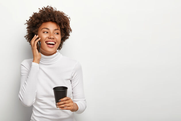 咖啡满意的无忧无虑的女人的照片 卷发 通过智能手机交谈 看起来积极的一边 喝外卖咖啡 在活泼的交谈中心情很好人和生活方式饮料通话通信