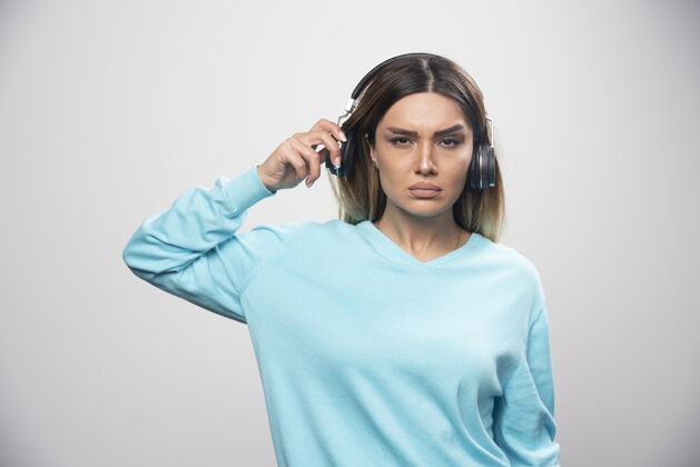 人穿着蓝色运动衫的金发女孩戴着耳机试图听懂音乐中立休闲仔细
