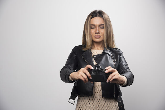 人类穿着黑色皮夹克的年轻女士认真专业地用相机拍照设备女人年轻人