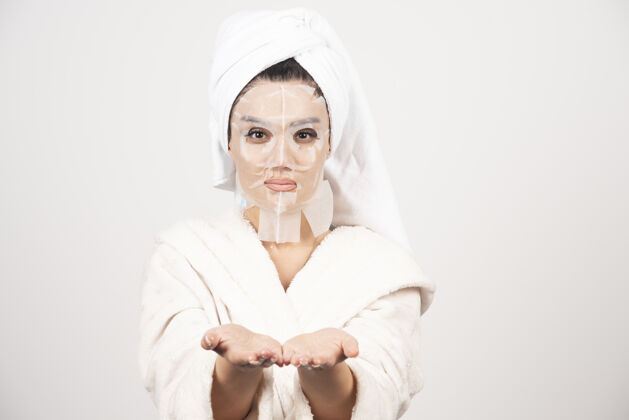 漂亮穿着浴衣和带面罩的毛巾的女人护理清洁面部
