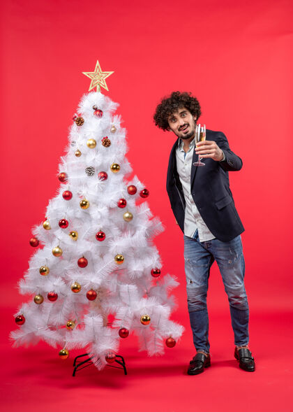 圣诞树新年庆祝与年轻人拿着一杯葡萄酒附近装饰白色圣诞树上的红色镜头圣诞酒年轻人