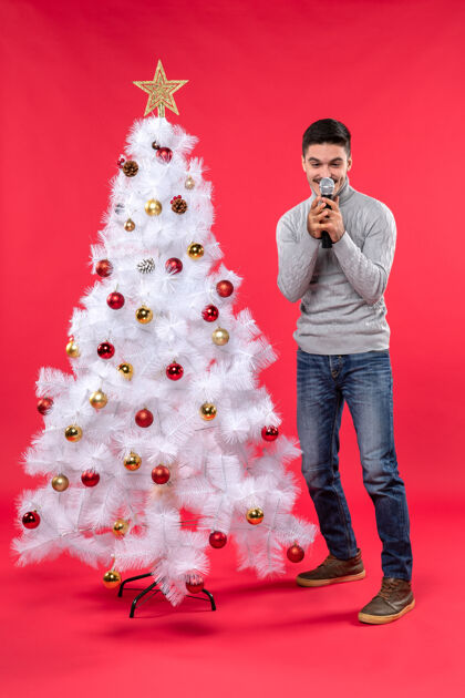 心情新年心情带着微笑积极的家伙穿着牛仔裤站在红色装饰的圣诞树旁站立礼物圣诞节