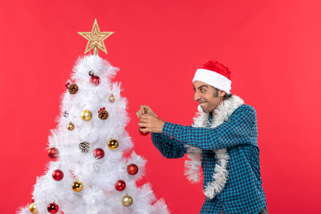 衬衫滑稽的年轻人戴着圣诞老人的帽子 穿着一件蓝色的衬衫 手里拿着圣诞树雪人圣诞节