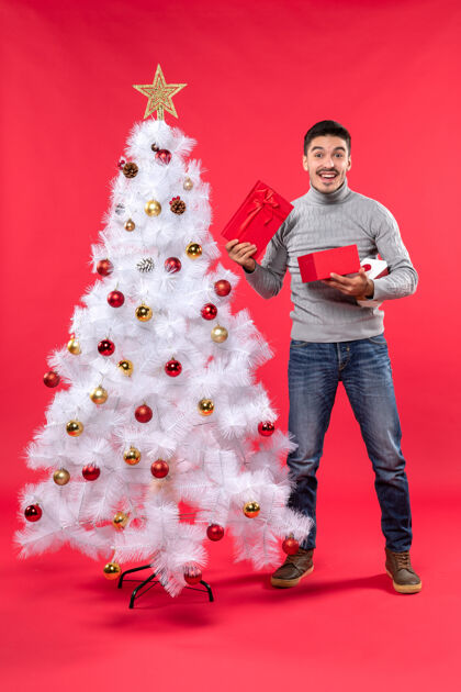 长袜俯视图微笑英俊的成年人穿着灰色衬衫站在装饰白色圣诞树附近上衣礼物开幕式