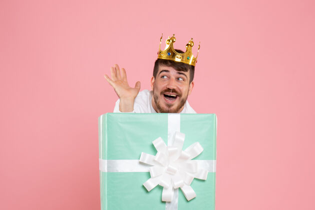 微笑年轻人在礼物盒内的正面视图 粉红色墙上有皇冠帽子礼物年轻