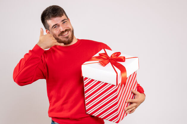 成人前视图中的年轻人在红衫举行圣诞礼物盒在白色的墙壁上快乐男性人