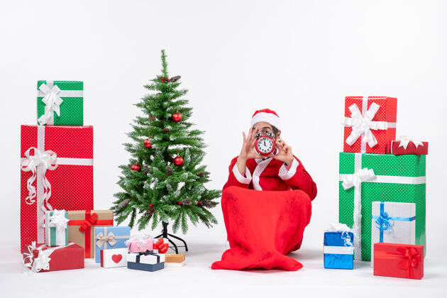 举行年轻人坐在地上 拿着钟 在礼物和装饰过的圣诞树旁庆祝圣诞节年轻人庆祝礼物