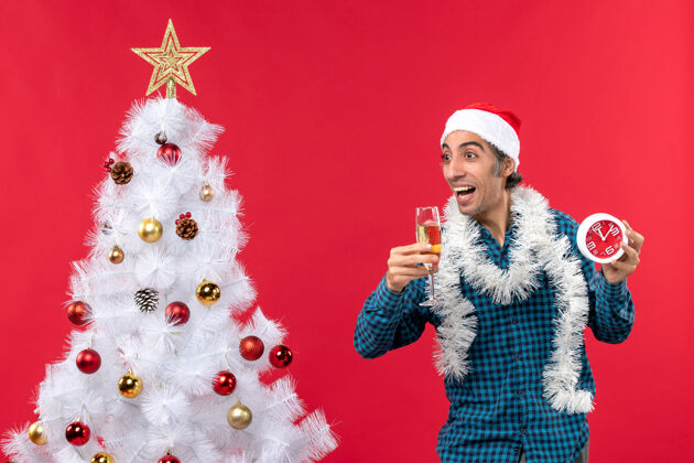 圣诞一个带着圣诞老人帽子 拿着一杯酒和一个闹钟的疯狂的情绪化的年轻人庆祝杯子钟