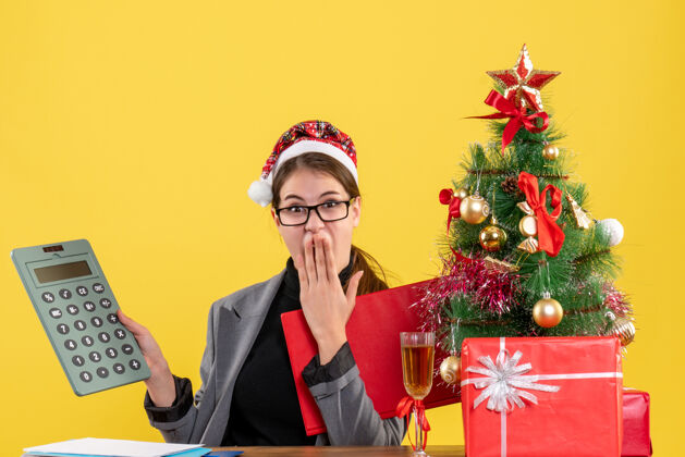 桌子前视图震惊的女孩戴着圣诞帽坐在桌子旁看着计算器放在手上人震惊女孩帽子