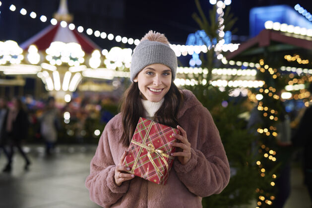 携带圣诞集市上拿着礼物的女人的画像温暖冬天户外