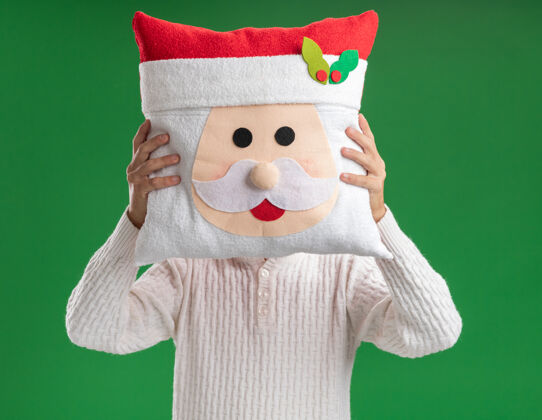 脸年轻帅哥戴着圣诞老人头带戴着眼镜抱着圣诞老人枕头在脸前隔离在绿色背景上头带枕头年轻人