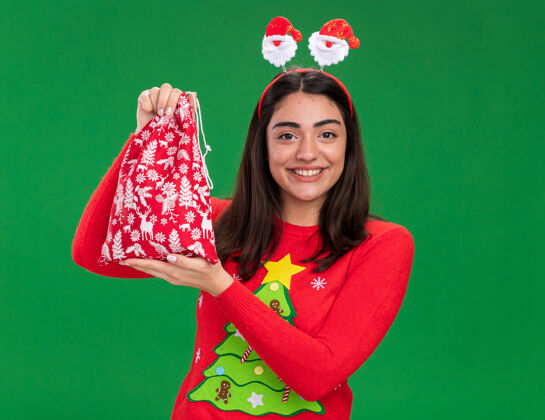 圣诞节高兴的年轻白人女孩与圣诞老人头带举行圣诞礼品袋绿色背景与复制空间隔离礼物头带包