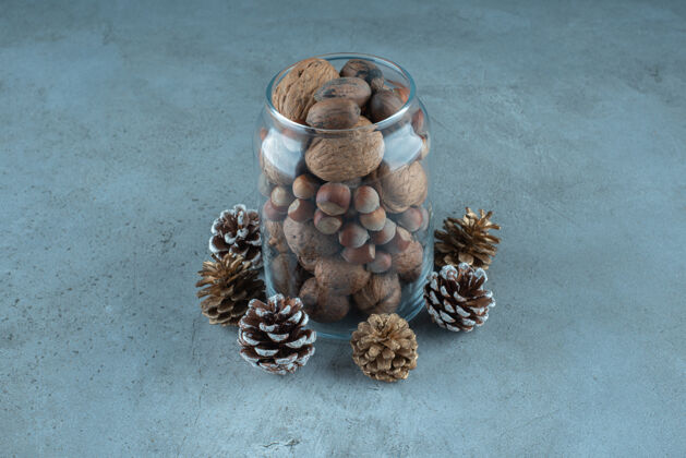 干的一个装满各种坚果的罐子放在大理石表面的松果旁边榛子什锦的松子