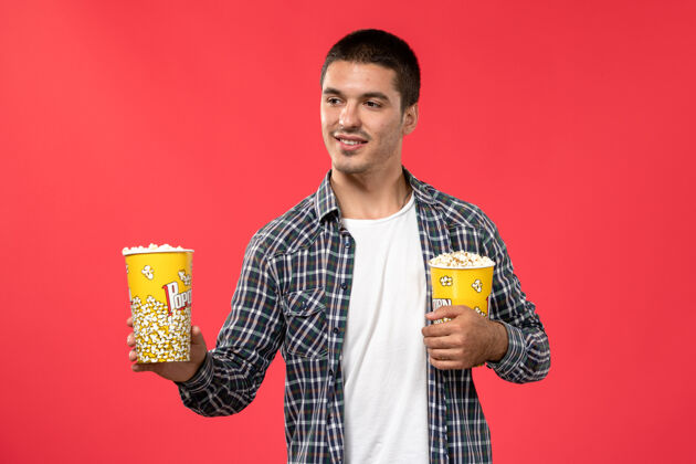 包装正面图年轻男子拿着爆米花包在浅红的墙上电影院看电影浅红色电影院西装