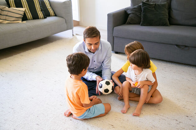 姐姐关心的爸爸拿着球 给孩子们讲故事白人中年爸爸和孩子们坐在客厅的地板上 一起玩耍童年 游戏活动和父亲的概念地毯女儿爸爸