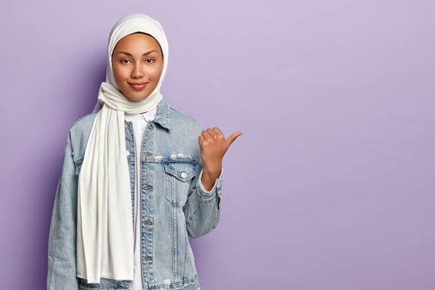 牛仔身着传统阿拉伯服装的迷人女性 拇指指向右侧 在空白处呈现物体 有宗教观点 孤立于紫色墙壁之上宗教概念摆姿势宗教