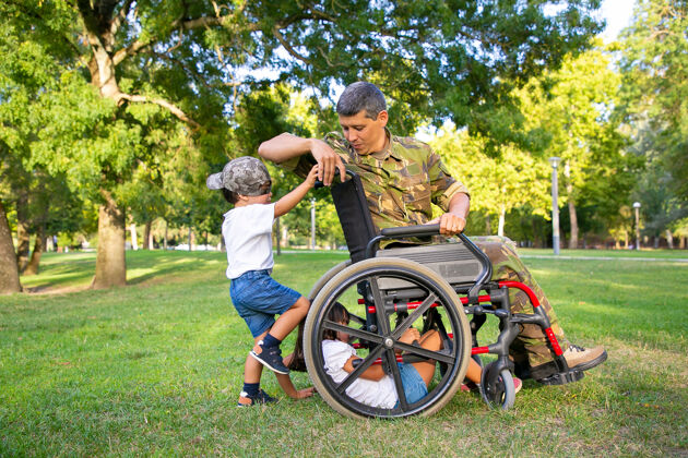 白种人积极的残疾军人爸爸在公园里和孩子们一起享受时光孩子们在草地上玩轮椅退伍军人或残疾概念侧长度完整