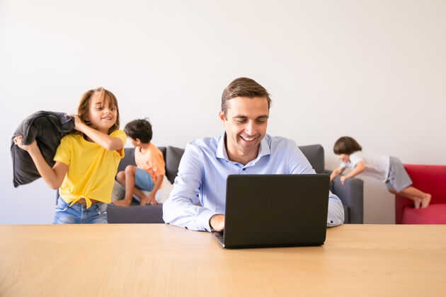 童年快乐的爸爸通过笔记本电脑聊天 孩子们在他身边玩枕头高加索父亲在学校假期在家工作家庭和数字技术概念生活男孩朋友
