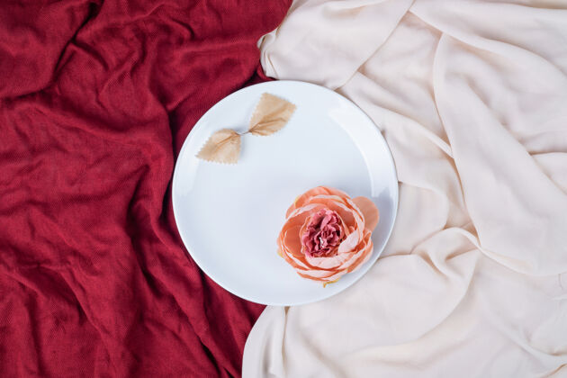 摆设白色盘子上的一朵花 红色和粉色桌布玫瑰盘子花