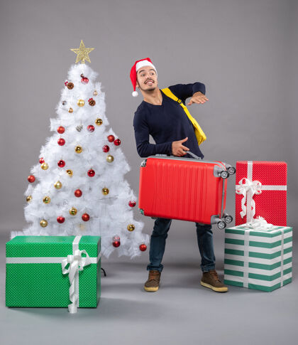 圣诞在灰色隔离带上观察那个拿着红色手提箱的年轻人购物红色服装