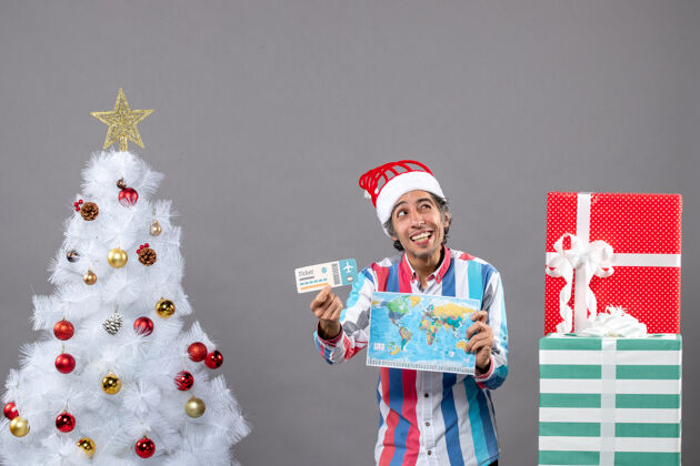 圣诞树正面图微笑的男人眨着眼睛拿着世界地图和旅行票眼睛旅行者快乐