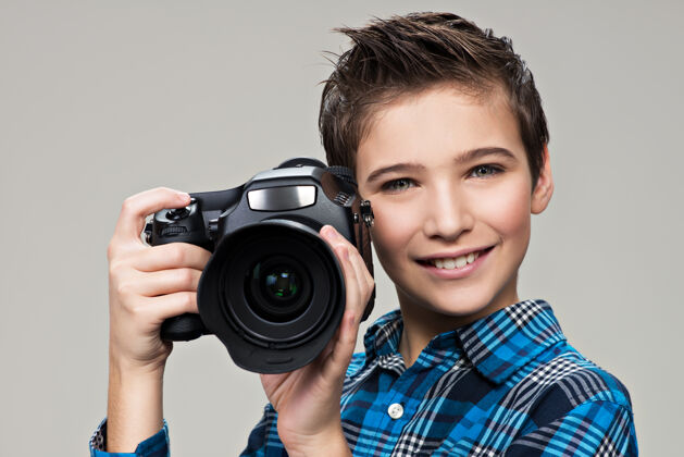 男性男孩拿着相机拍照高加索男孩的肖像 手里拿着数码相机摄影师拍摄灰色背景