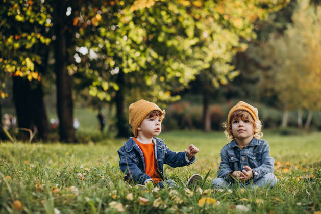 休闲两个男孩兄弟坐在树下的草地上坐着孩子帽子