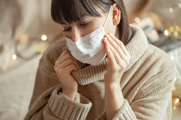 冠状病毒穿着舒适的米色毛衣 脸上戴着面具的年轻女子冬天感染面具