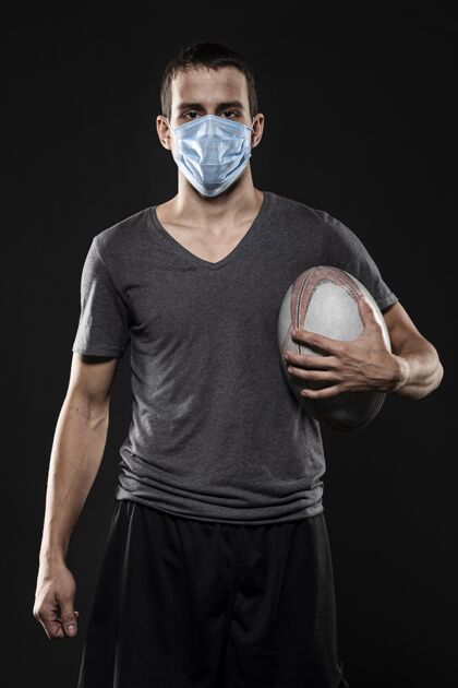 球员男橄榄球运动员戴着医用面罩拿着球的前视图比赛竞技医疗面罩