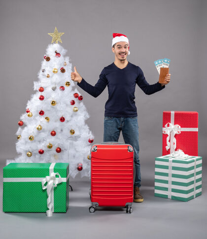 灰色一个带着红色手提箱的惊讶的男人张开双手 手里拿着灰色的旅行票包圣诞老人圣诞