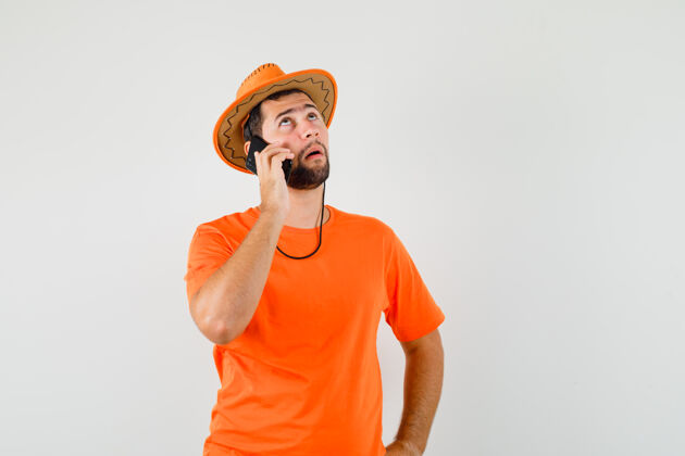 时尚身穿橙色t恤 戴着帽子 面带沉思地用手机交谈的年轻人前视图模特工作室男性