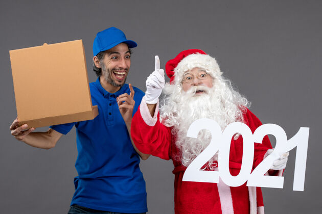 盒子圣诞老人的正面图 男信使拿着食物盒 站在灰色的墙上服装节日人