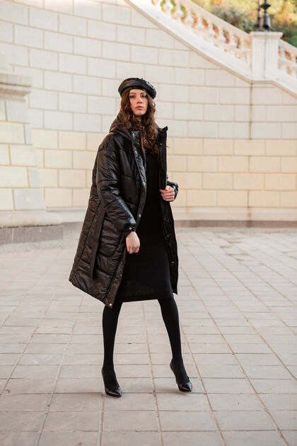街头时尚女人摆出冬秋时尚潮流黑色羽绒服和皮帽贝雷帽在古老美丽的街道穿着高跟鞋女性时尚街头风格