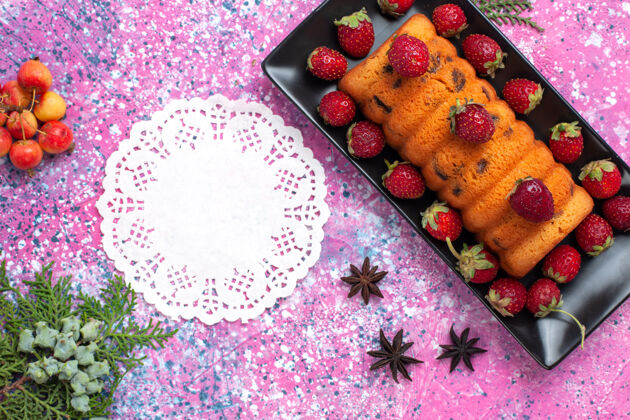 关闭顶部近距离观看美味的烤蛋糕在黑色的蛋糕锅里 粉红色的桌子上放着新鲜的红色草莓花水果饼干