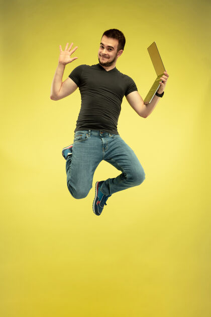 肖像快乐跳跃的人与黄色背景上隔离的小玩意全长肖像现代技术 自由选择的概念 情感的概念使用笔记本电脑的工作和飞行乐趣手男性电脑