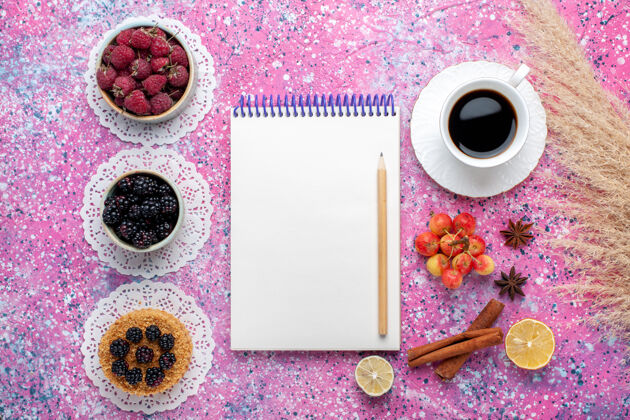 浆果顶视图小黑莓蛋糕与新鲜的覆盆子和黑莓茶在淡粉色的桌子上浅粉色小花