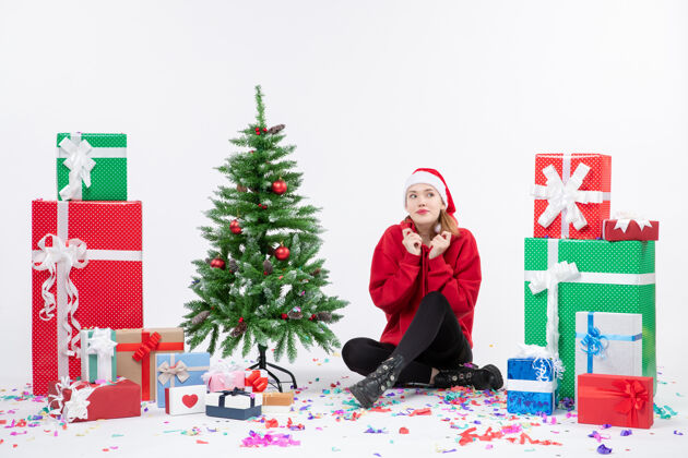 快乐年轻女子围坐在白色墙壁上的礼物前视图十二月季节性礼物