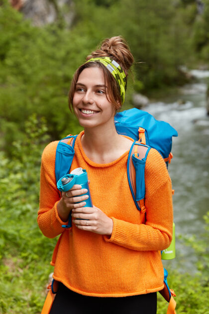 乐观高兴的年轻女游客有非凡的徒步旅行 享受热饮 持有烧瓶积极高兴积极