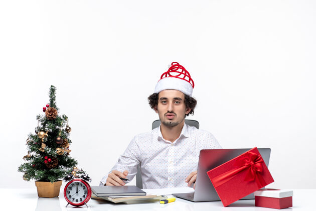 成年人满足忙碌的年轻商人与有趣的圣诞老人帽子检查书写笔记和庆祝圣诞节在白色背景的办公室圣诞节年轻人检查