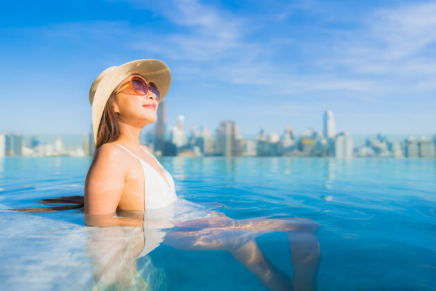 高美丽的亚洲年轻女子在户外游泳池周围放松 城市景色尽收眼底梦想城市顶部