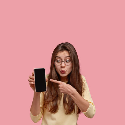 凝视震惊的黑发女士合影 用食指指指在手机模拟屏幕上 展示出惊人的东西Omg设备惊呆了