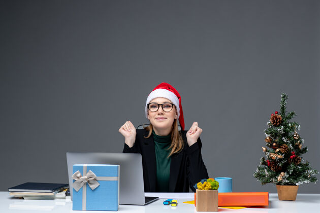 圣诞老人在办公室里 一位年轻漂亮的女士戴着圣诞帽坐在一张桌子旁 桌上放着圣诞树和一份礼物桌子帽子电脑