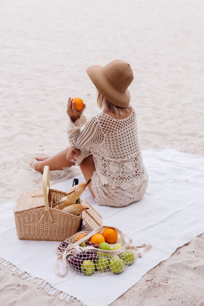 复制空间一个年轻的女人坐在毛巾上 戴着草帽 穿着白色针织衣服和野餐篮子篮子吸引人空间